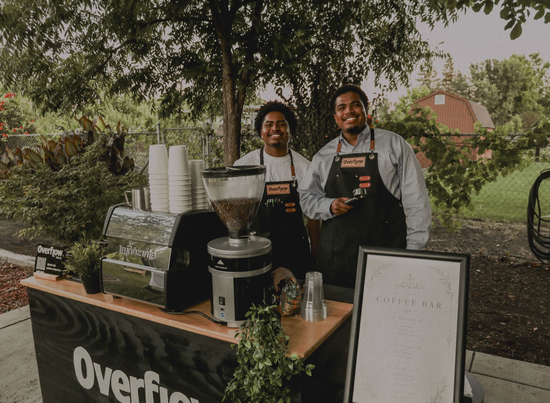 Two Overflow Coffee Co. baristas smiling behind their outdoor espresso cart